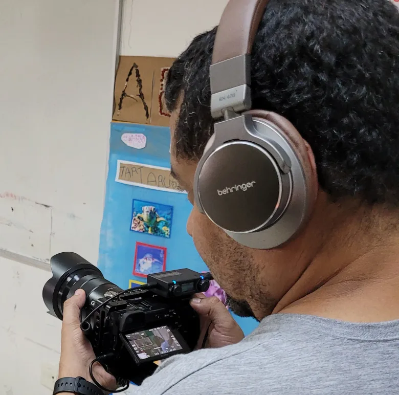 Professor de fones filmando com câmera durante a oficina de audiovisual